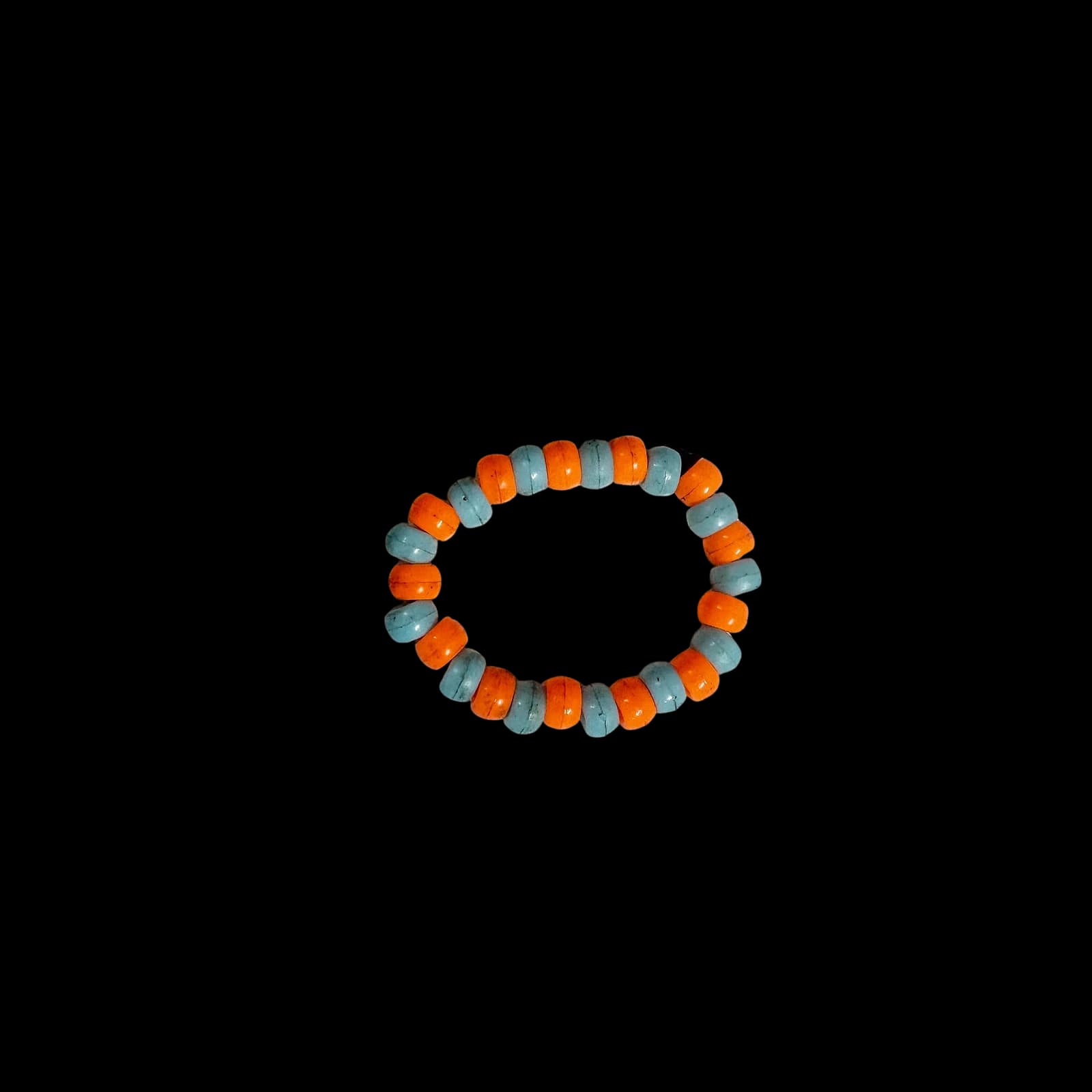 Handmade bracelet with alternating orange and light blue beads on a black background.